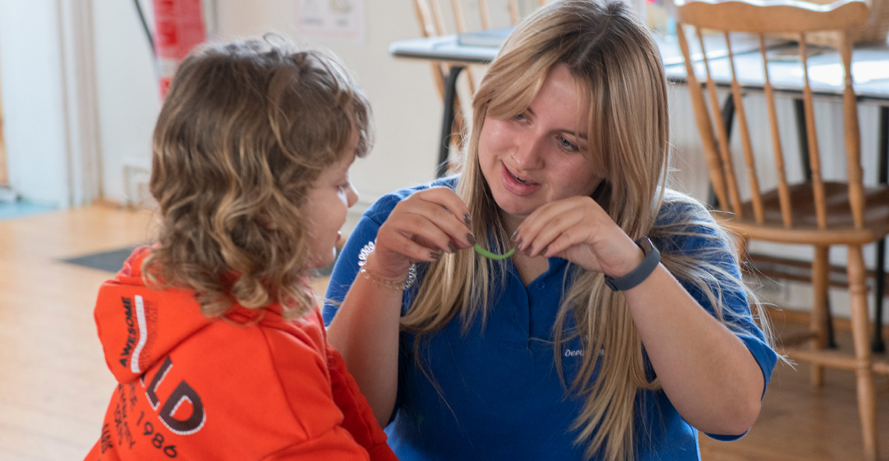 An education worker holding a piece of plasticine and talking to a child